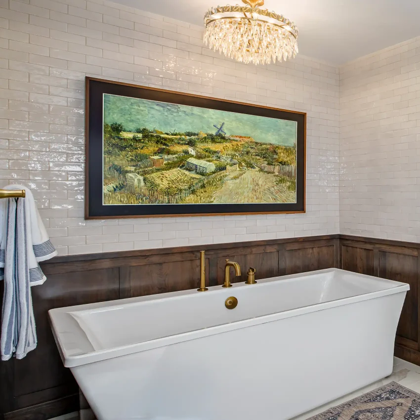 Bathroom with a crystal chandelier, wainscoting, freestanding tub and brass fixtures