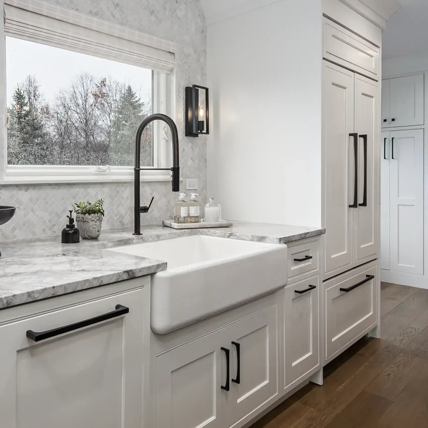 Chic white kitchen design featuring farm sink, black high arch faucet and Quartzite countertops.