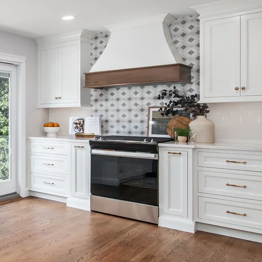 White kitchen cabinets with a geometric backsplash and wood range hood